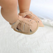 Beige baby shoes with woven design on a white background