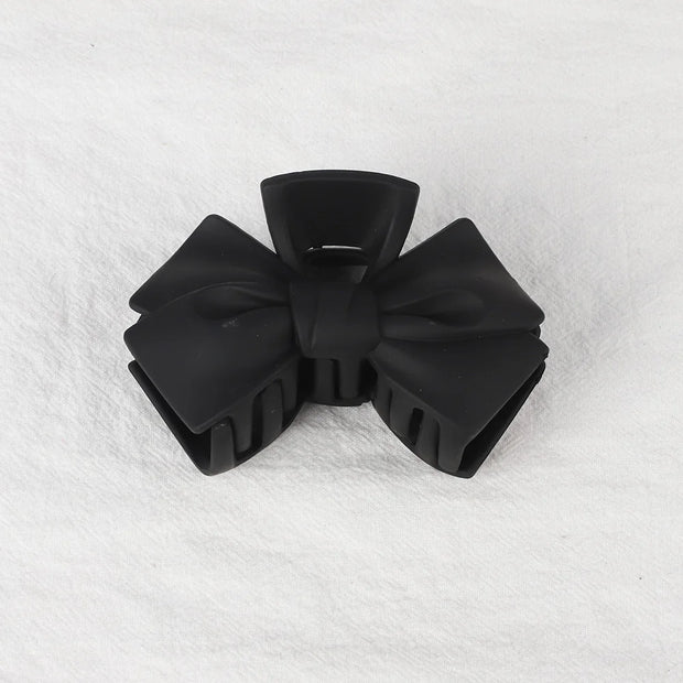 Black bow-shaped hair clip on a white textured background