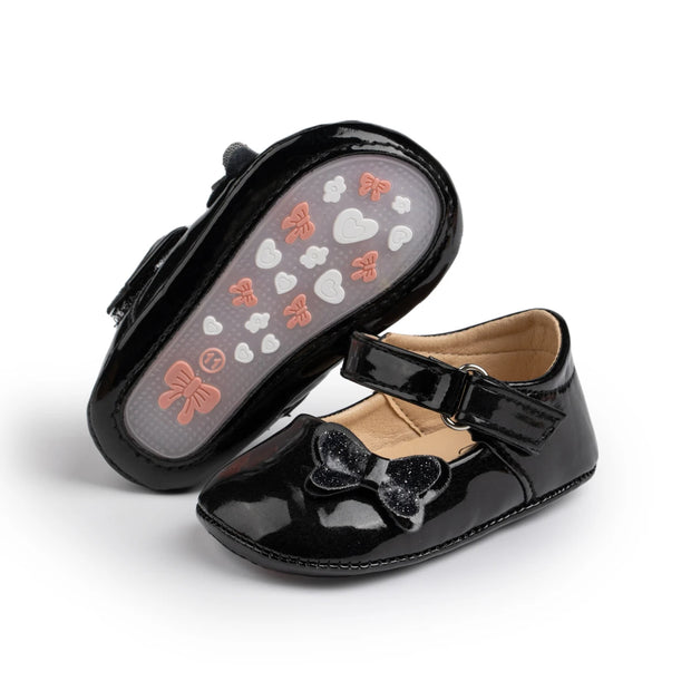 Black patent leather shoes with bow details on a white background