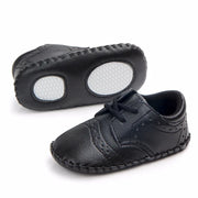 Pair of black baby shoes with white soles on a white background