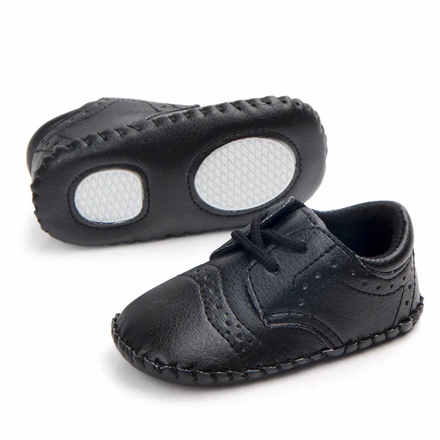 Pair of black baby shoes with white soles on a white background
