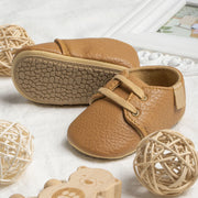 Pair of brown leather baby shoes on a light surface with decorative elements.