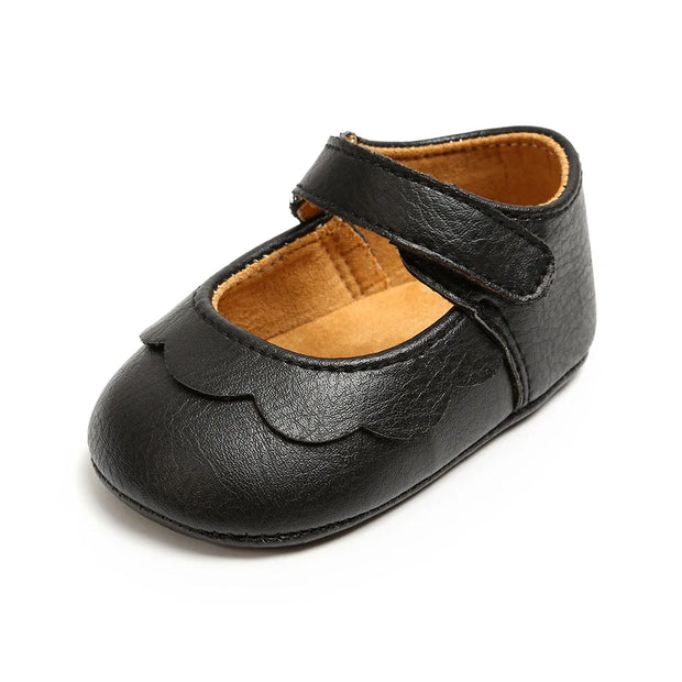 Black leather baby shoe with a strap on a white background