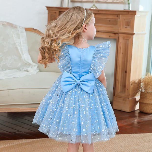 Young girl in a blue dress with a large bow standing in a living room.