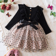 Black long-sleeve top with ruffles and a beige polka dot dress on a textured surface.