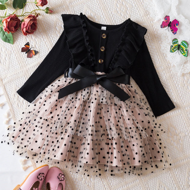 Black long-sleeve top with ruffles and a beige polka dot dress on a textured surface.