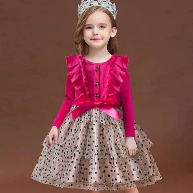 Young girl wearing a pink top and polka dot skirt with a tiara on a brown background