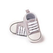 Pair of gray baby sneakers with white laces on a white background