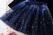 Navy blue tulle skirt with star patterns and a large bow on a textured surface.