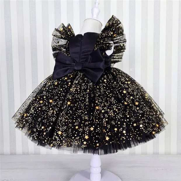 Black tulle dress with gold stars and a large bow on a mannequin against a white background