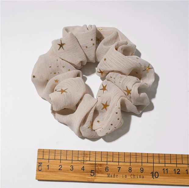 Beige scrunchie with gold stars on a white background, next to a wooden ruler for size reference.