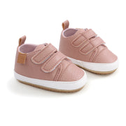 Pair of pink baby shoes with white soles on a light background
