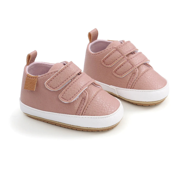Pair of pink baby shoes with white soles on a light background