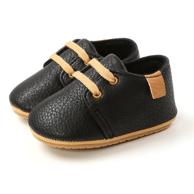 Black leather shoes with tan laces and accents on a white background