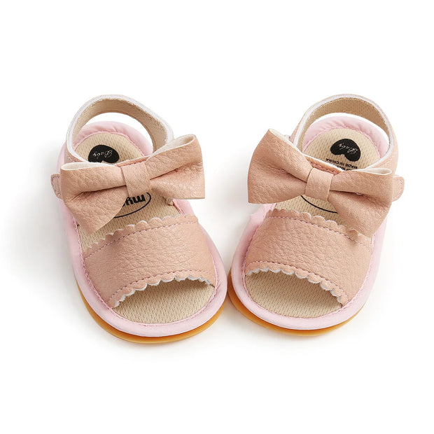 Pair of pink baby sandals with bow details on a white background