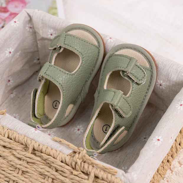 Pair of green baby sandals on a textured fabric surface