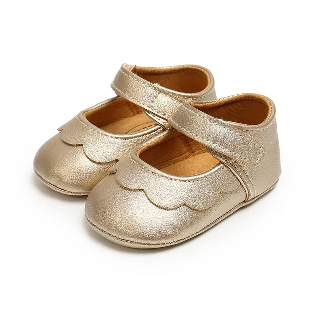 Pair of gold baby shoes with scalloped edges on a white background