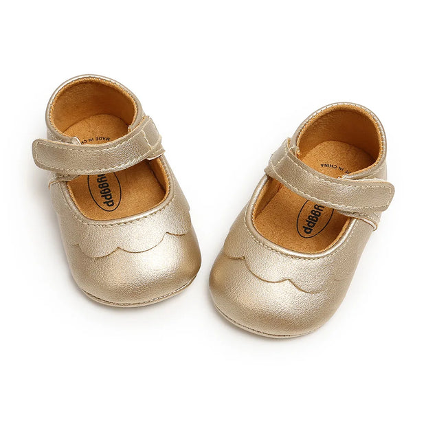 Pair of gold baby shoes with a strap on a white background