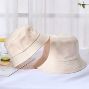 Two beige bucket hats on a white surface with a light curtain background.