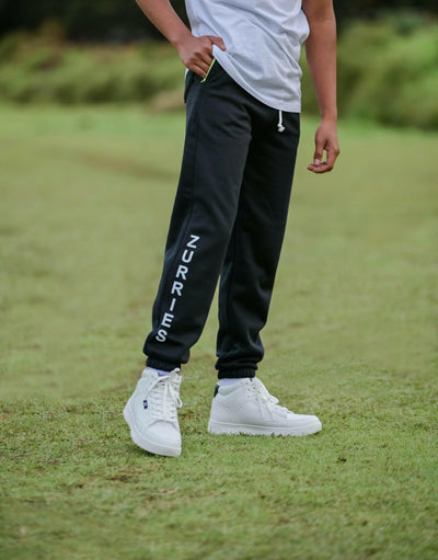Person wearing black jogger pants with 'Zurries' branding on a grassy field.