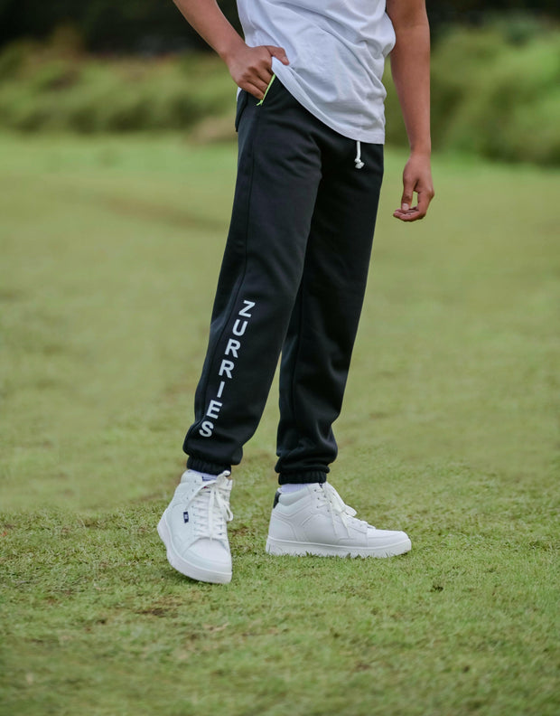 Person wearing black jogger pants with 'Zurries' branding on a grassy field.